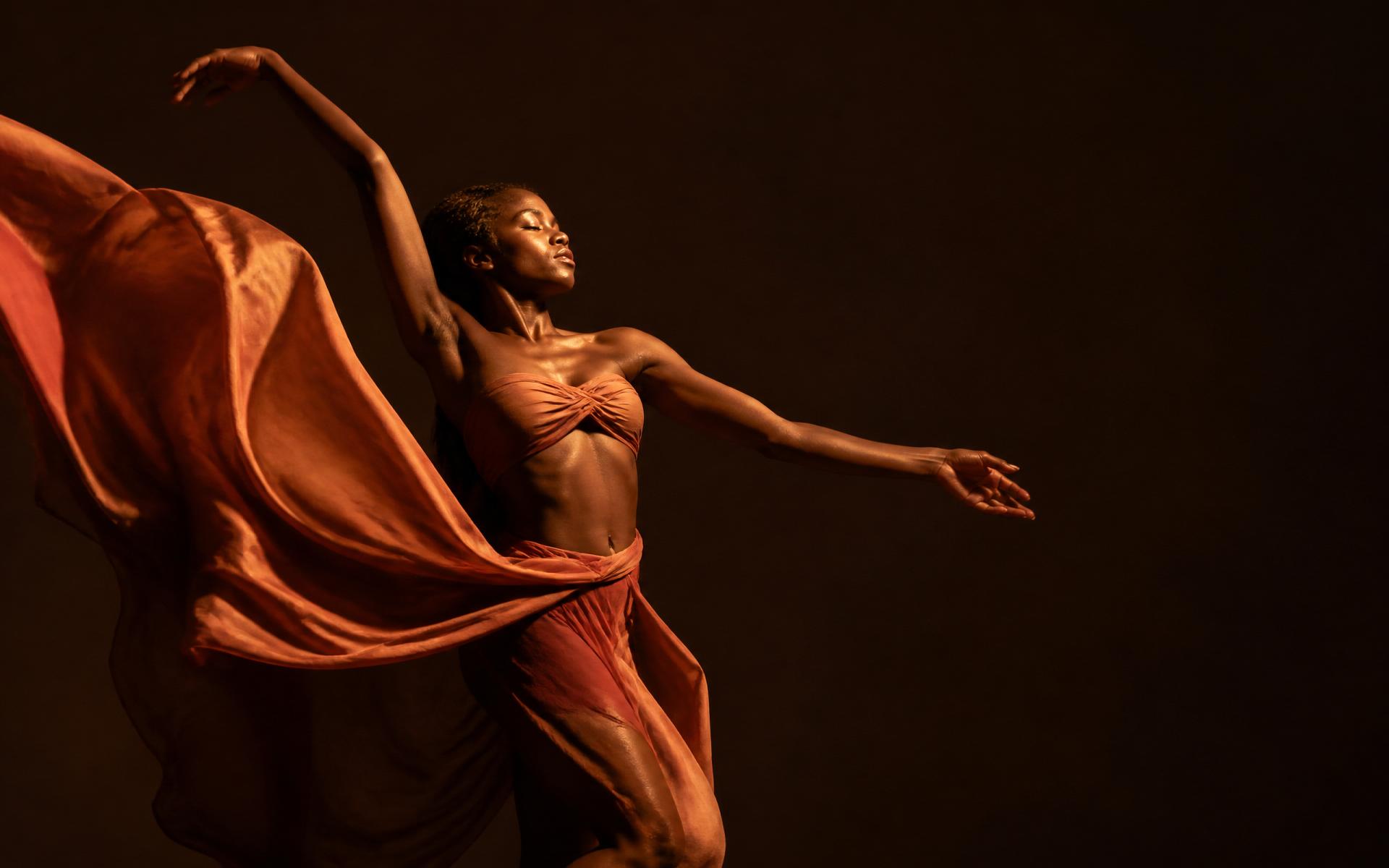 Afro-contemporary dancer mid-motion in terracotta fabric